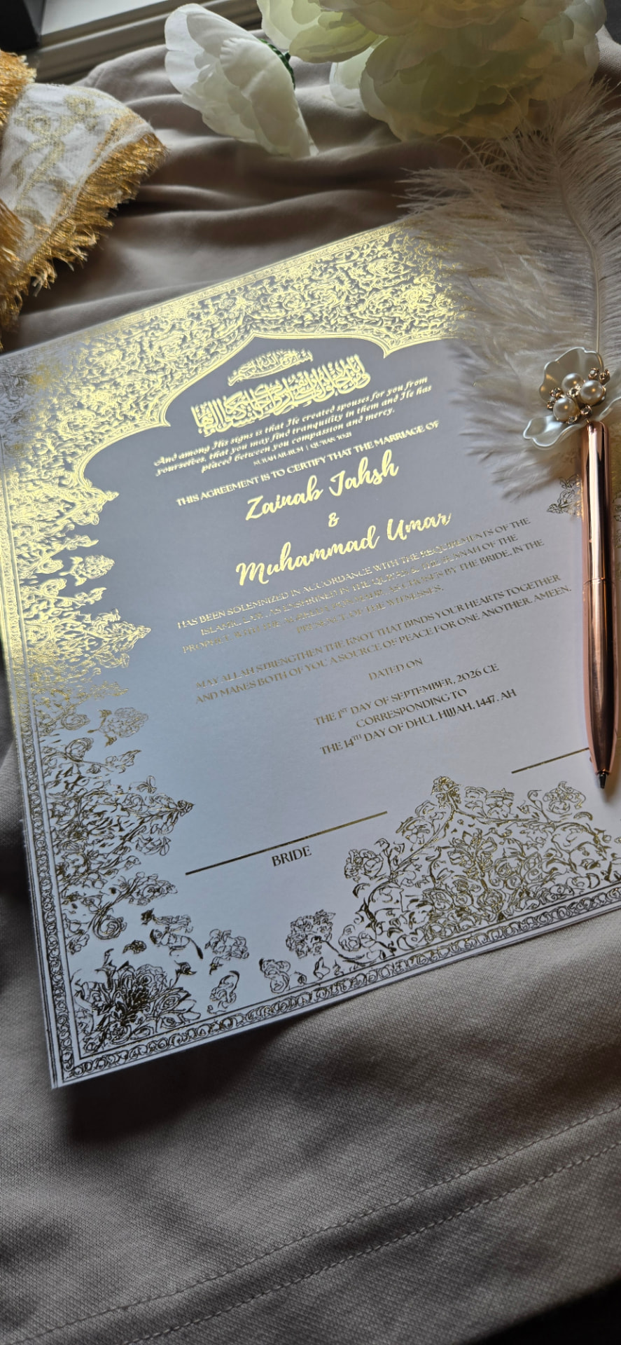 A Nikah certificate with gold foil detailing, framed with a feather pen and florals